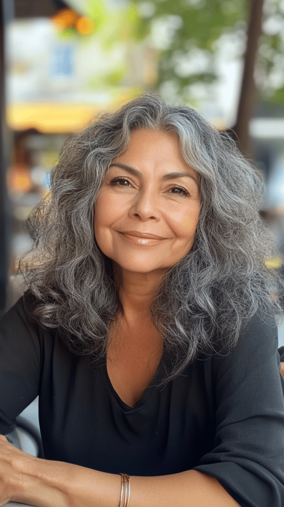 A 60-year-old Latina woman with big, bouncy curls full of volume, sitting at an outdoor café table.