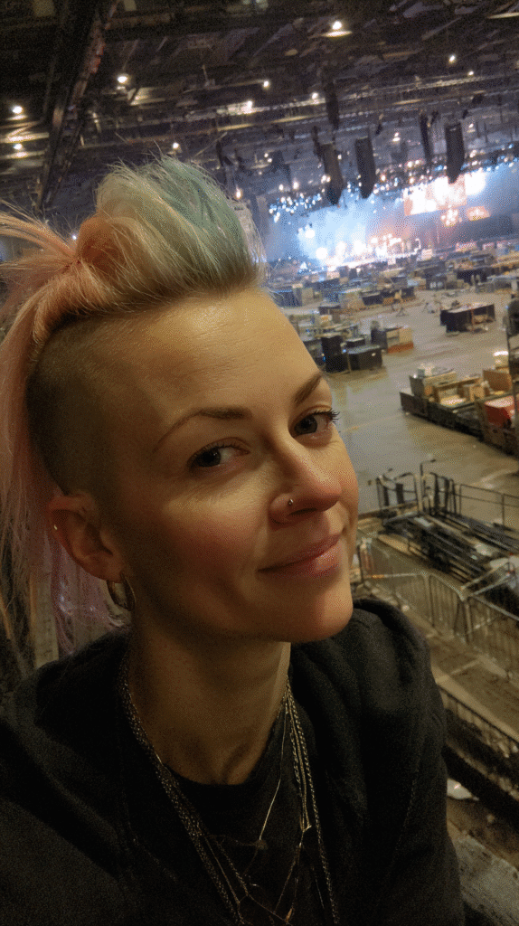 A 29-year-old woman with a tall mohawk and bleached ends, styled in a warehouse concert venue.