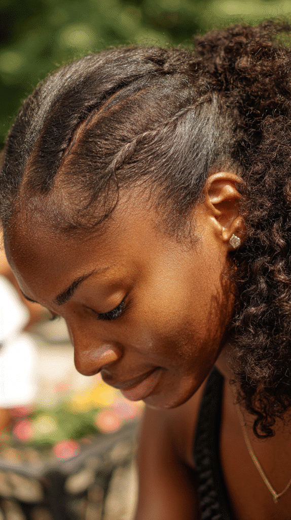 Black woman wearing side ponytail with neatly styled cornrow accents feeding into curly lengths.